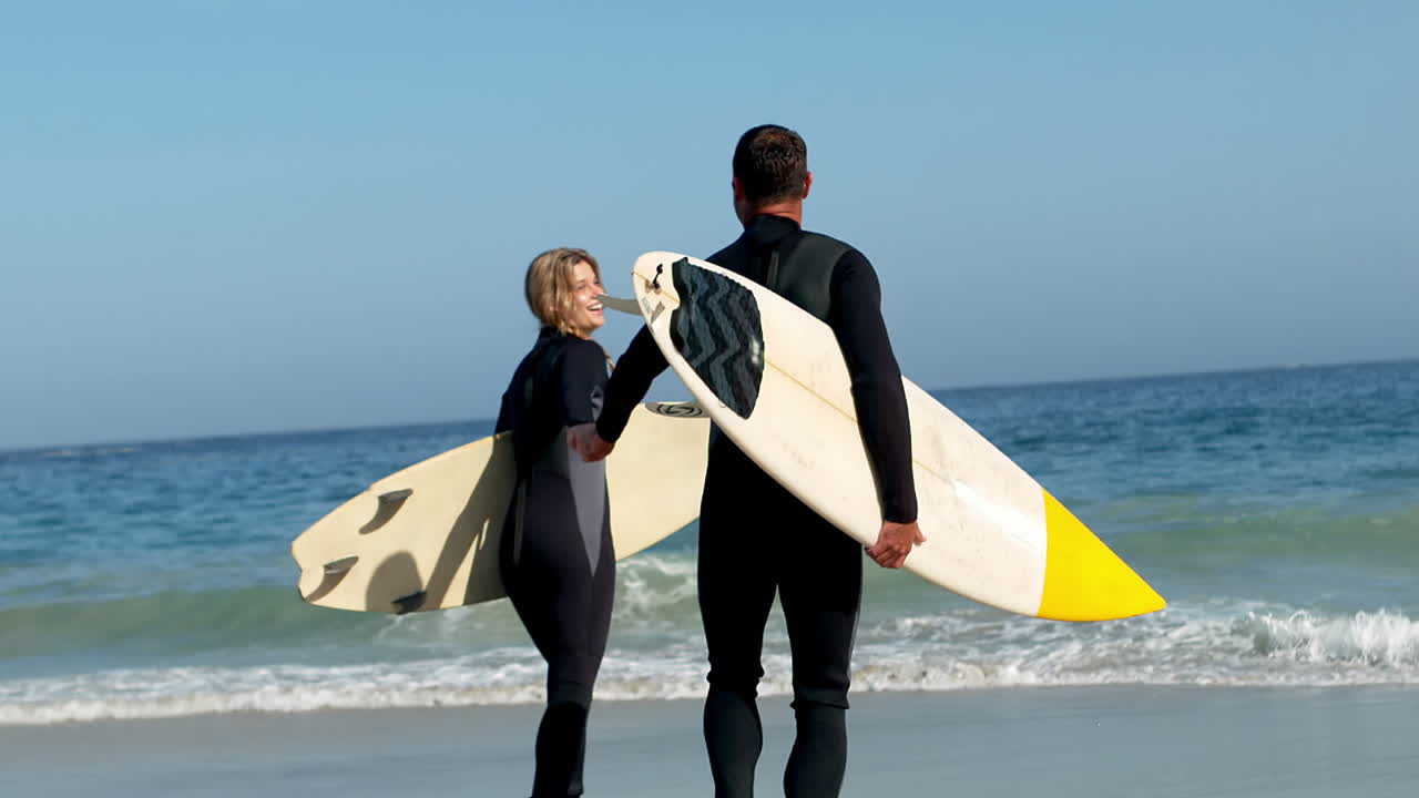 pareja corriendo hacia el agua con una tabla de surf