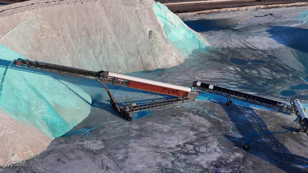 Panning drone video of conveyor pouring bright blue salt on pile near railcars on railway tracks in Detroit site