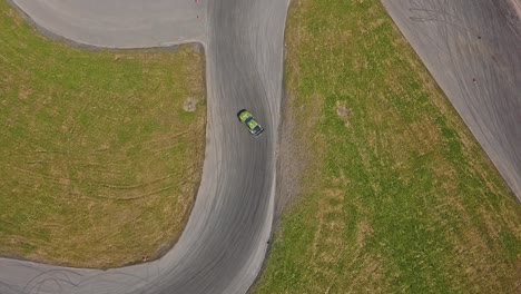 toma aérea de un automóvil a la deriva a alta velocidad en un giro, hierba verde y una pista de carreras, toma de vista superior