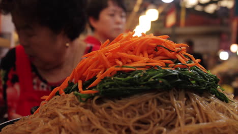 korean stir-fried noodles with carrots and vegetables at a market