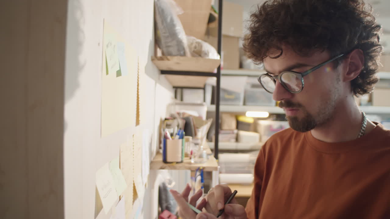 Man Writing on Sticker Attached to Wall in Workshop