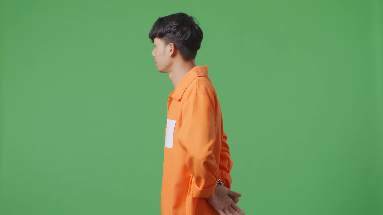 손을 은 아시아 남성 수감자가 녹색 스크린 배경에 서서 머리를 흔들며 자신이 한 일에 화를 내고 있습니다.