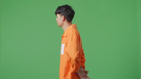 손을 은 아시아 남성 수감자가 녹색 스크린 배경에 서서 머리를 흔들며 자신이 한 일에 화를 내고 있습니다.