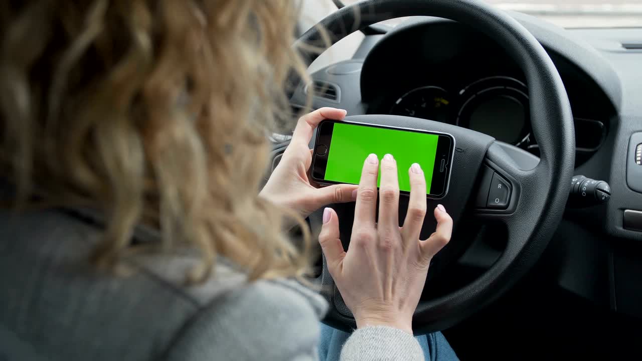 mujer se sienta en el coche moderno y trabaja en el teléfono inteligente - pantalla verde - primer plano