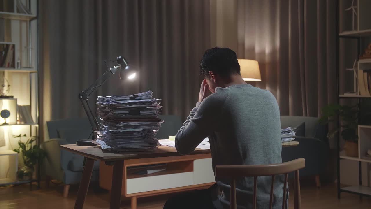 Back View Of Tired Asian Man Shaking His Head While Working Hard With Documents At Home