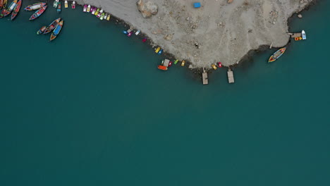 Vista-Aérea-Superior-Sobre-La-Orilla-Del-Lago-Attabad-Con-Coloridos-Barcos-Y-Casas