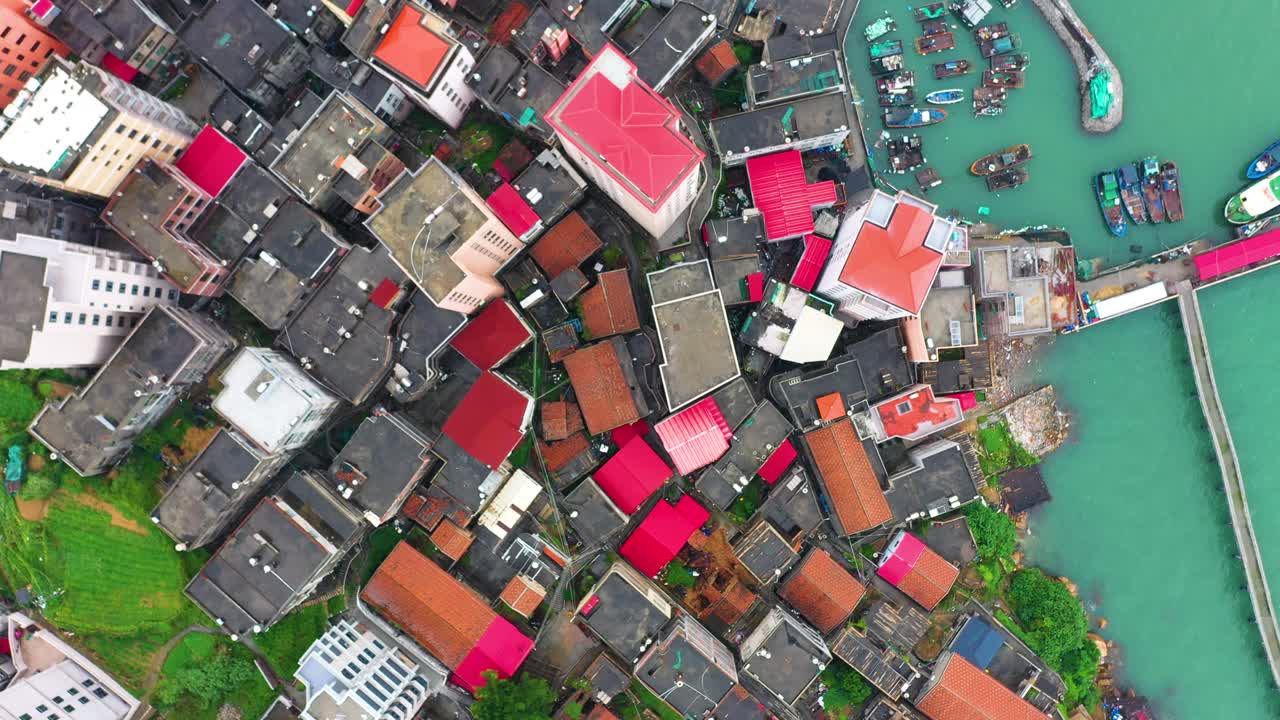 Aerial view of Gaobei Island in Putian City, Fujian Province, China, showcasing a densely built residential area with vibrant rooftops near a bustling harbor filled with fishing boats.