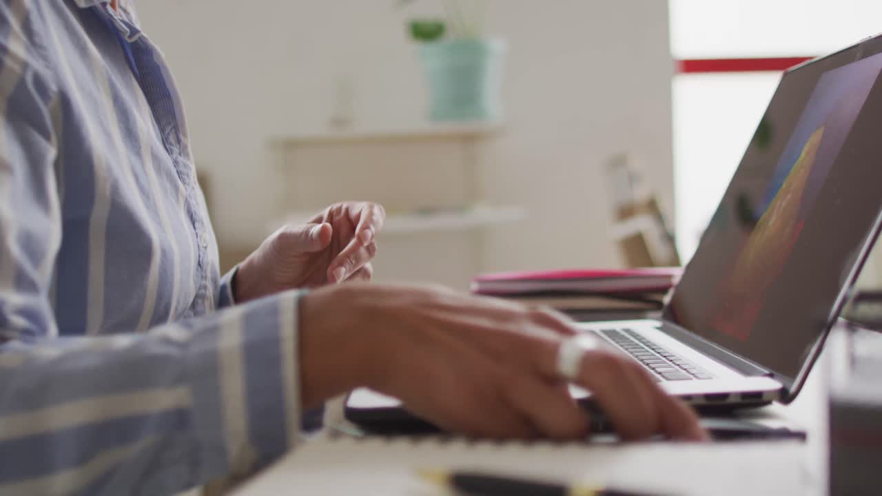 Video of midsection of biracial female designer working on laptop in studio