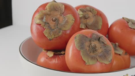 Panning-close-up-of-asian-persimmons-in-a-bowl-showing-stems-and-vibrant-color