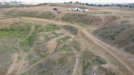 toma aérea de la pista de motocross en malaga españa con pista polvorienta y espectadores en las colinas mientras un motociclista da un giro y realiza un truco peligroso