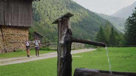 a young couple hikes past a wooden fountain in the lush robanov kot valley, slovenia