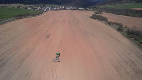 aerial drone rises above vast soil field, tractor carrying rollers to flatten