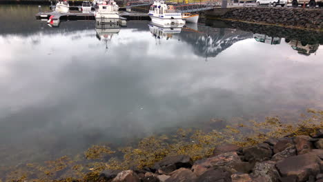 wasserreflexionen von bergen, booten und autos, die dann boote in einem kleinen hafen freigeben, umgeben von schneebedeckten bergen