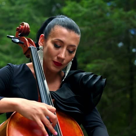 cello in woman's hands outdoors. beautiful woman with earrings and black dress playing the musical instrument on nature background.