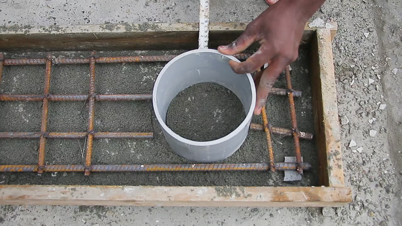 Indian mason worker accurately measuring distance of a plastic cylinder over sand from edge of a wooden slab with rebar grid