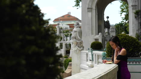 Asiatische-Frau,-Die-Auf-Renaissancebalkon-Steht-Und-In-Notizbuchzeitlupe-Aufschreibt