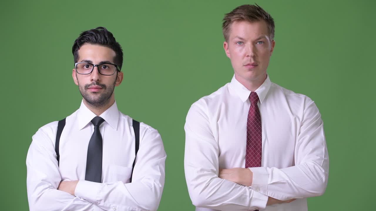 Dos jóvenes empresarios multiétnicos trabajando juntos sobre un fondo verde.