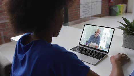 Back-view-of-african-american-woman-having-a-video-call-with-male-colleague-on-laptop-at-office