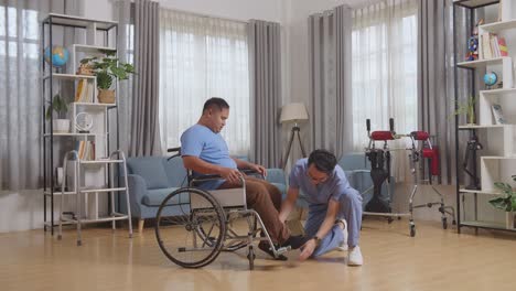 vista lateral del cuerpo completo de una enfermera masculina asiática ayudando a un paciente en silla de ruedas poniendo los pies en el reposapiés después de una terapia física en casa
