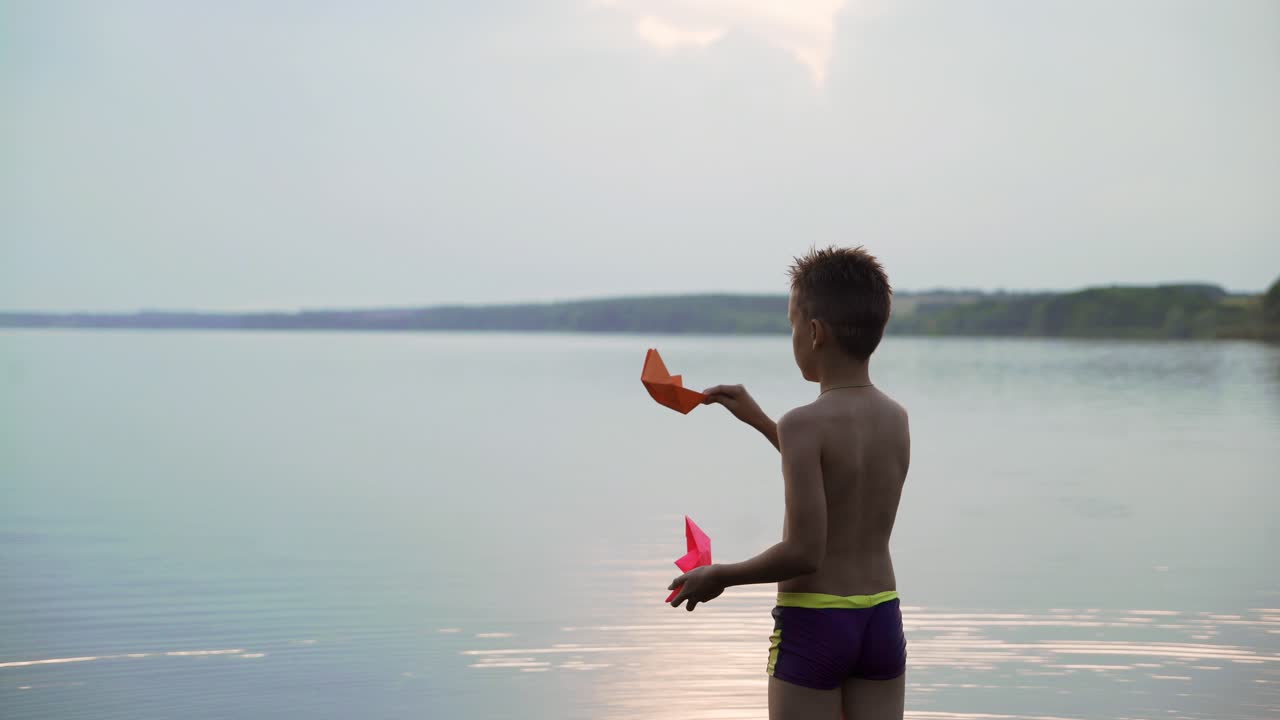 Little boy launch paper boats on the beach in summer. A child starts up a paper boat. Origami ship. Sailing.