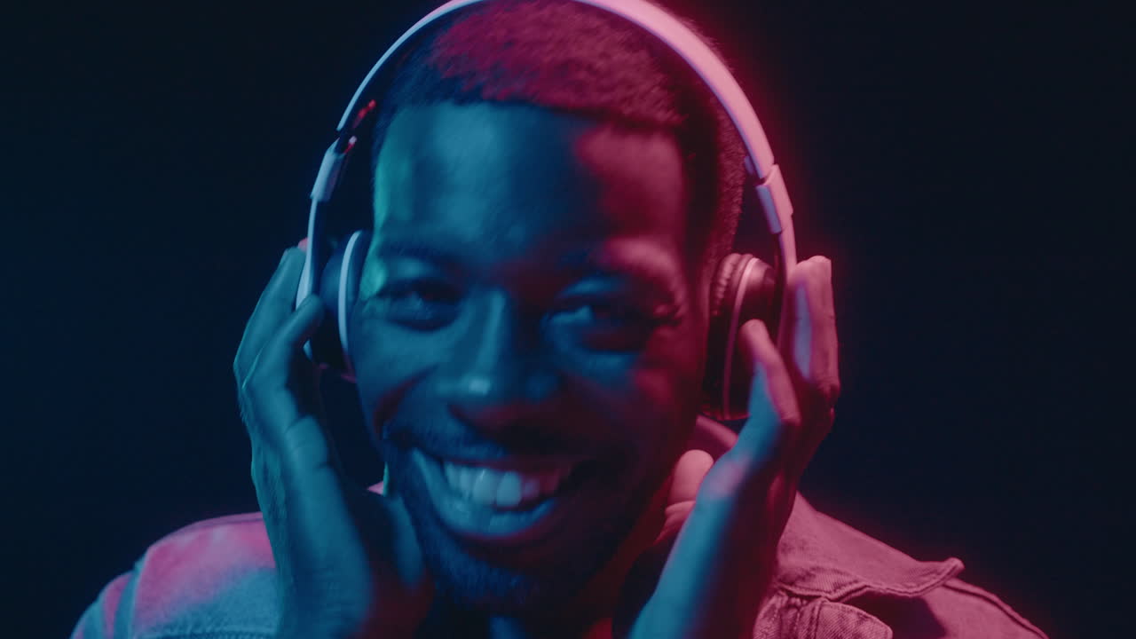 Cheerful Black Man in Headphones Dancing Under Neon Lights