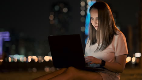 Joven-Y-Hermosa-Diseñadora-Trabajando-Remotamente-En-Una-Computadora-Portátil-En-La-Calle-En-Verano-Bajo-Palmeras-Por-La-Noche-En-El-Parque-De-La-Ciudad.-Emiratos-Árabes-Unidos-Mujer-Europea-En-La-Noche-En-Dubai