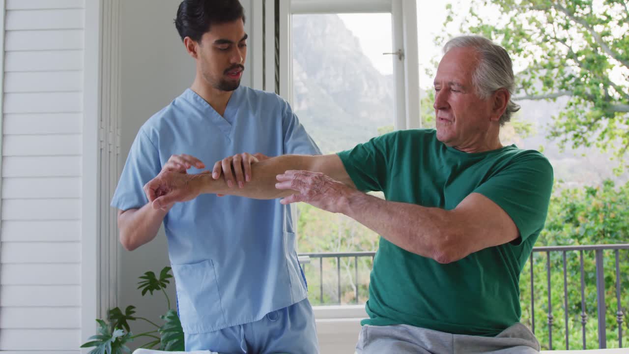 Slow motion of biracial male physiotherapist examining retired senior man's arm at nursing home