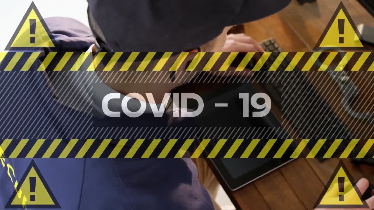 Video composito digitale di testo Covid-19 con un segnale di avvertimento giallo su uno sfondo di una guardia di sicurezza uomo che usa il computer.