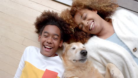 portrait of happy african american mother and son lying on floor, with their pet dog, slow motion