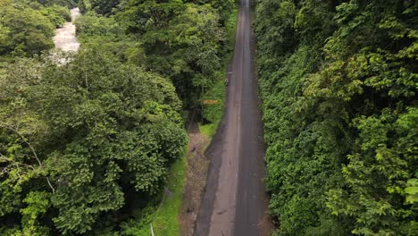 Aufsteigender-Drohnenschuss-Eines-Jungen-Mannes,-Der-Während-Der-Regenzeit-Auf-Einem-Motorrad-Am-Rand-Einer-Dschungelstraße-In-Costa-Rica-Sitzt