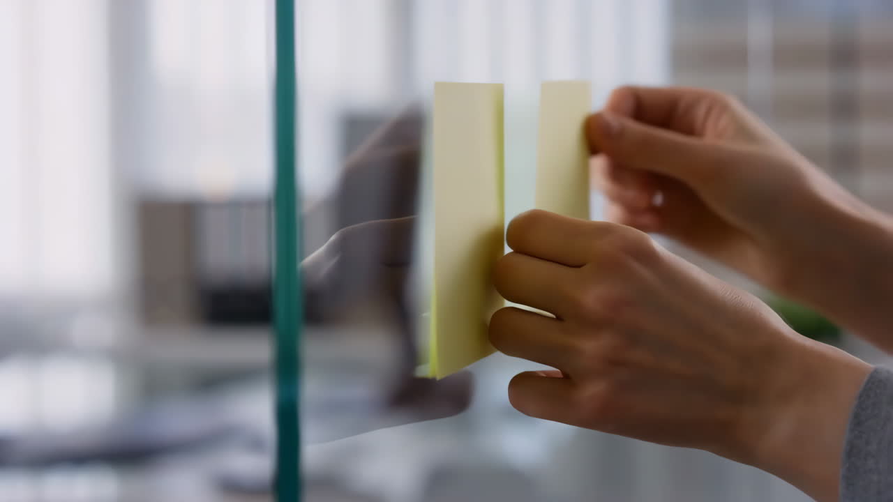 Hands placing sticky notes on a glass board