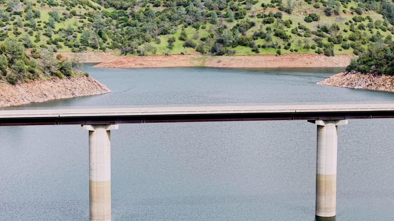 Overhead perspective of a car traversing the Don Pedro Reservoir Bridge, with the calm reservoir reflecting sunlight.