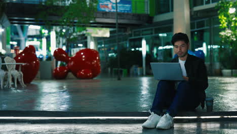 man working on a laptop in a city at night