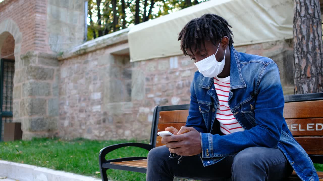 African teenager with a mask playing phone