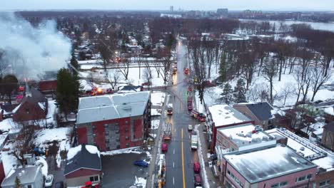 Luftaufnahme-Von-Rauch,-Der-Im-Winter-Aus-Einem-Gebäude-Mit-Feuerwehrautos-Auf-Der-Straße-Austritt