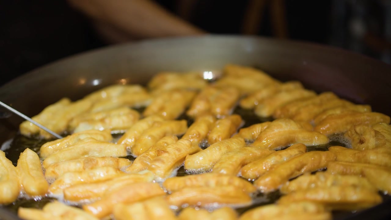 Primo piano di bastoncini di pasta patongko dorati che friggono in un grande wok di olio bollente