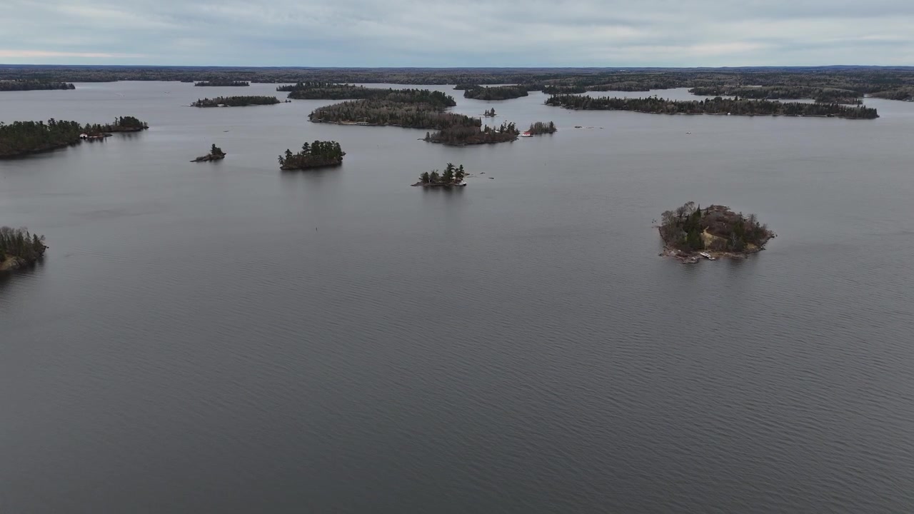 Lago dos Bosques perto de Kenora, Ontário. Drone aéreo voa para a frente sobre águas abertas em direção a ilhas distantes sob céus ensolarados de primavera com visibilidade clara e condições de lago calmas