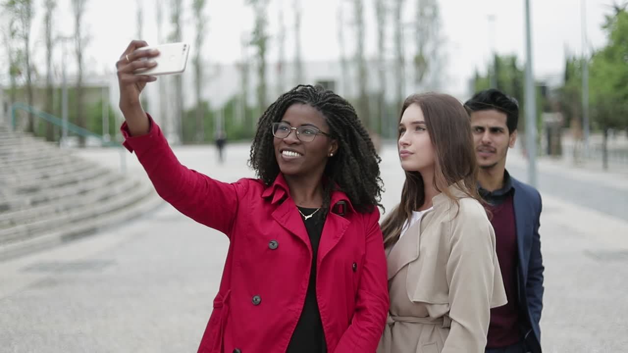 dos mujeres y un hombre haciendo una selfie afuera, posando, sonriendo