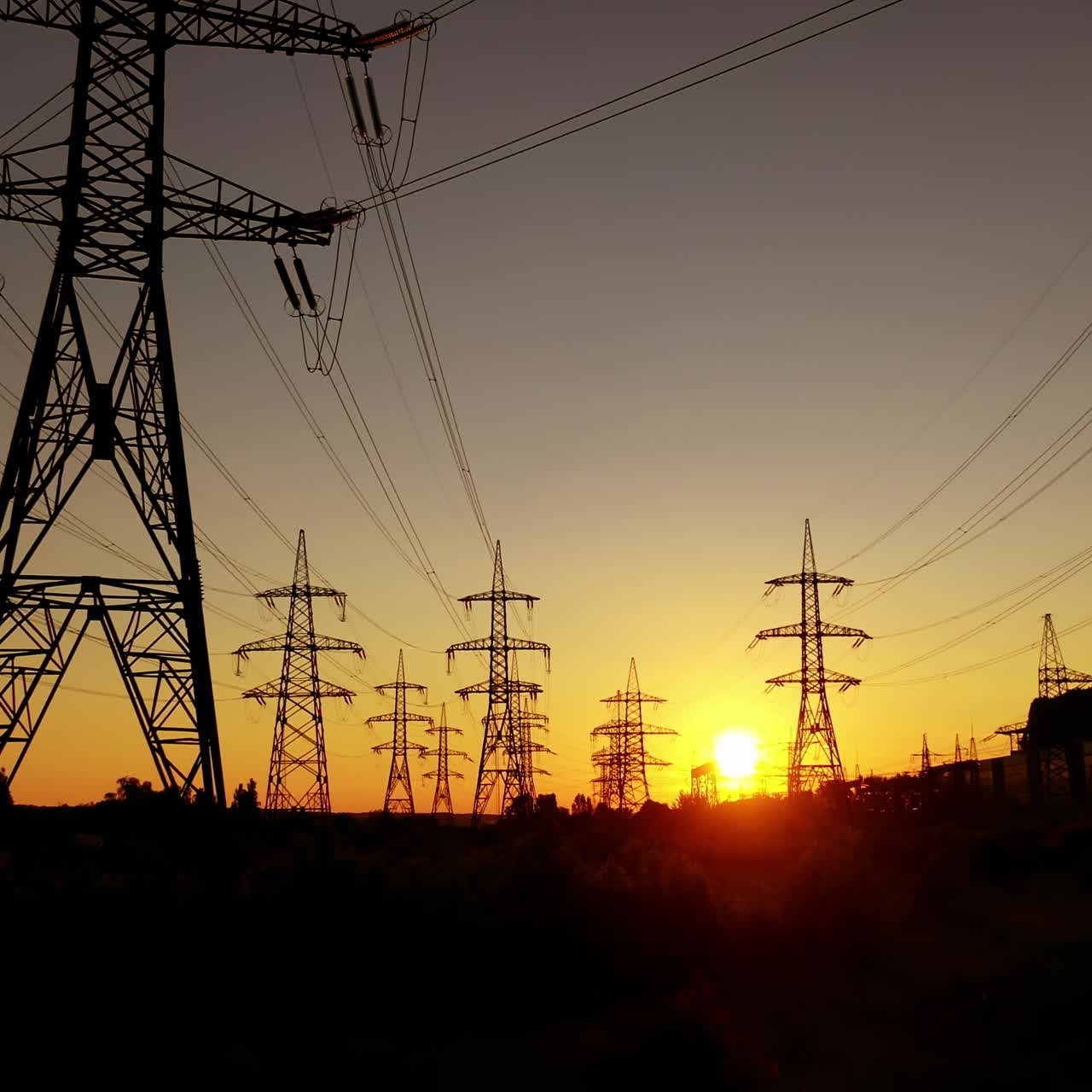 Transmission towers at orange sunset. Electricity pylons. Moving through electric high voltage pylon against the setting sun. Energy efficiency conception.