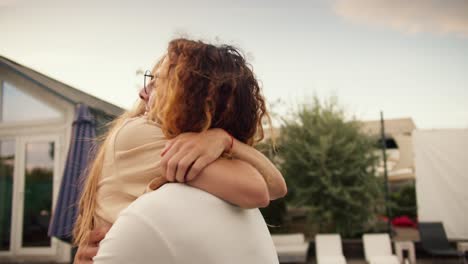 Close-up-shooting:-A-girl-with-long-hair-rides-her-curly-haired-boyfriend-in-glasses-and-hugs-him-near-the-sunbeds-by-the-pool.-Rest-in-the-country-house