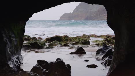 amazing closeup of natural rock arch window on beach coast with fog, sand, moss, pebbles and waves, porto santo island, madeira, 50fps hd