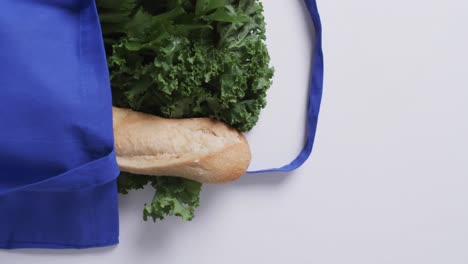 Video-of-blue-canvas-bag-with-parsley,-kale-and-baguette,-copy-space-on-white-background