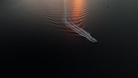 motorboat leaves wake in golden sunset beam on calm ocean water
