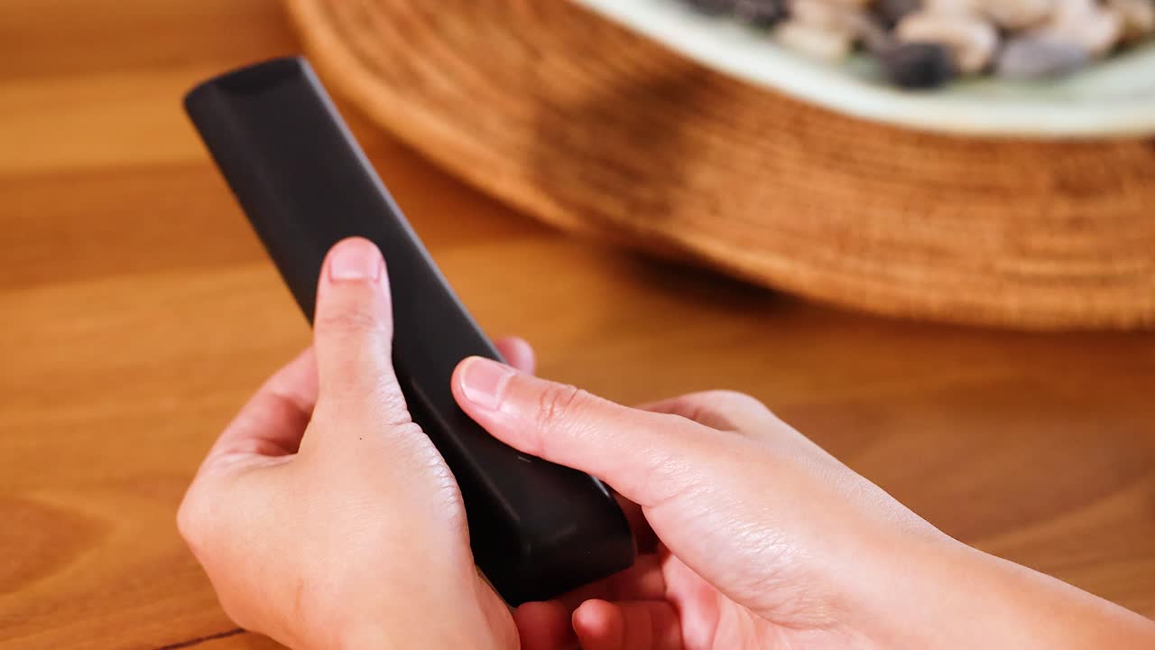 Hands replace a battery in a remote control on a wooden table with soft lighting