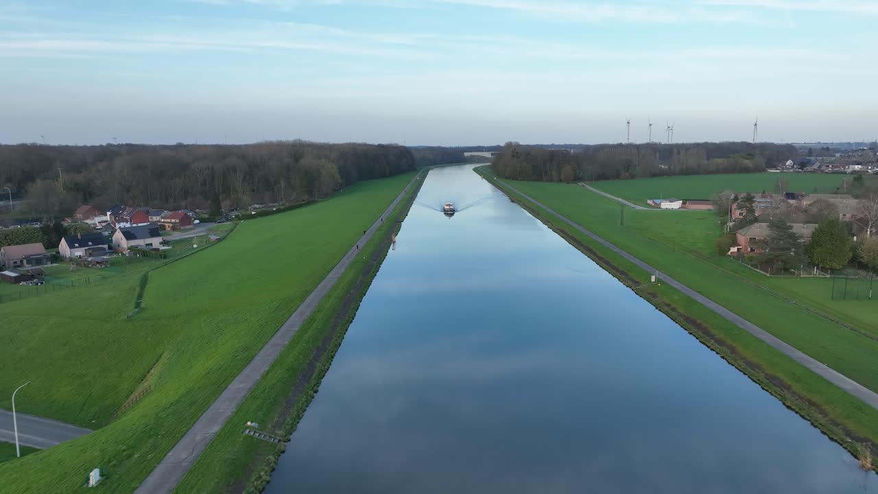 Aerial zoom in of a boat moving along the long straight elevated canal in Le Roeulx at golden hour