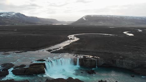 the extremely popular waterfall godafoss filmed from an aerial view showing the amazing surroundings of snowcovered mountains in the background and the river flowing in the rocky landscape