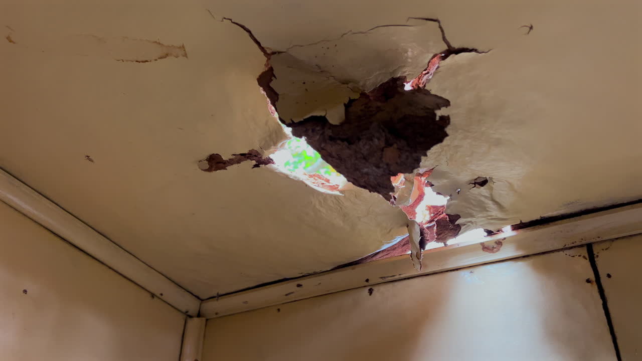 Soffitto danneggiato dall'umidità rivela buchi, crepe e luce diurna che filtra in un angolo interno