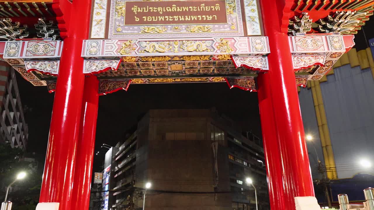 Camera tilts upward on illuminated Chinatown archway at night, wet ground reflecting city lights