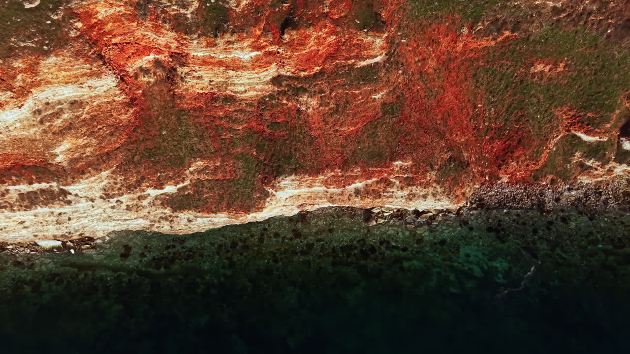Scogliere e acqua lungo la costa mostrano colori e motivi durante le ore di sole in un ambiente naturale vicino alla riva dell'oceano