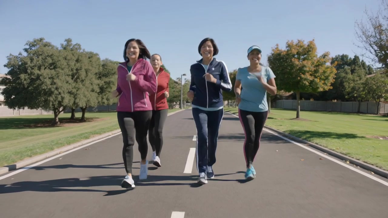 Gruppo di quattro donne che fanno jogging, stimolate dal sole, che si allenano su una strada suburbana, indossando giacche.